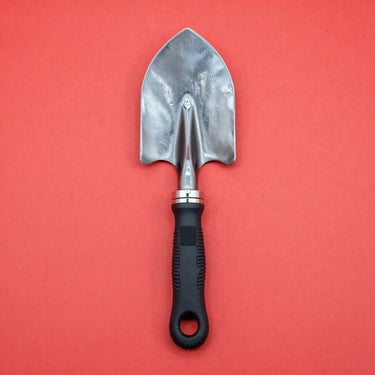 Centered flat-lay photo of a compact multi-tool camping shovel with survival gear on a clean red backdrop, crisp studio light