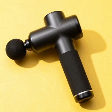 High-key studio shot of a sleek matte black muscle massage gun on a sunny yellow backdrop, crisp shadows, sharp focus