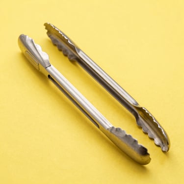 Close-up product shot of heavy-duty titanium magnetic grilling tongs, bright high-key lighting, vibrant yellow backdrop, sharp focus
