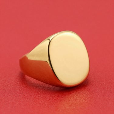 Dynamic close-up of a chunky gold signet ring on a bright red backdrop, high-key studio lighting, sharp focus