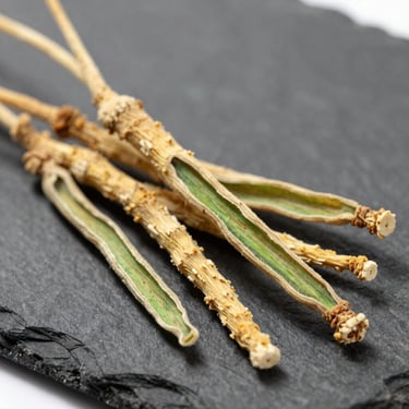 Macro close-up of raw dried Ashwagandha roots on a dark slate background, sharp focus, botanical precision, bright daylight