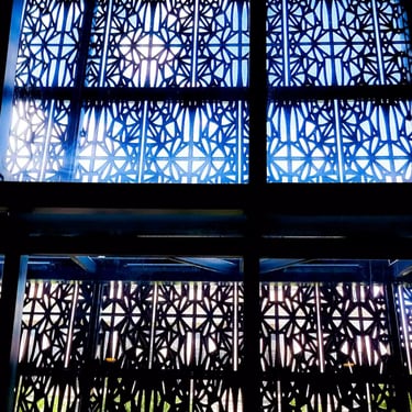 A colour photograph of a window’s intricate ironwork design with bright light streaming through it