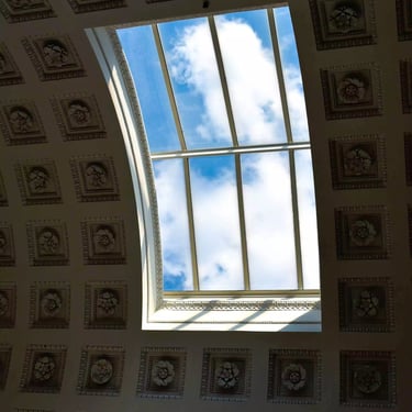 A colour photograph of an old European building’s overhead window with blue skies seen through it