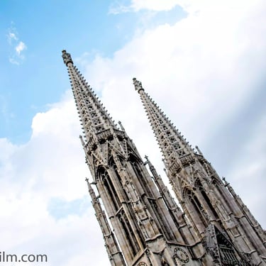 A colour photograph of a church’s two Gothic style towers set against a dramatic blue sky