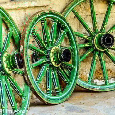 A colour photograph of three beautifully decorated green carriage wheels leaning against a rustic wall