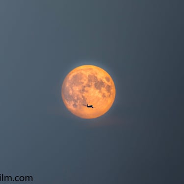 A colour photograph of an airplane backlit by a full moon 