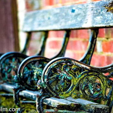 A close-up colour photograph of an old, weathered bench set against a red brick wall