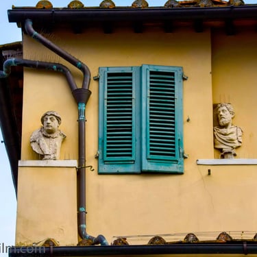 A photo featuring the upper section of a Mediterranean house decorated with two Roman style bust statues.