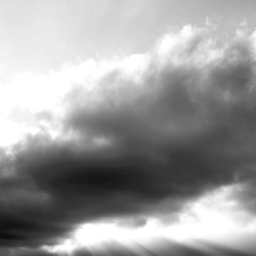 A black & white photo of rays of light breaking through thick and moody clouds