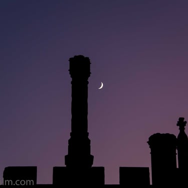 A photo featuring an intricate silhouette of classic architectural detail set against a vivid twilight sky & a crescent moon.