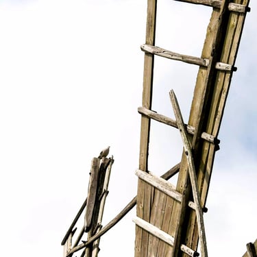A close-up colour photograph of an old windmill’s wooden blades set against a cloudy sky