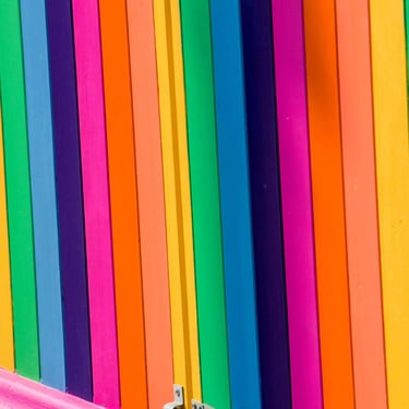 An abstract photograph of window shutters featuring an array of bold vertical stripes in a spectrum of vivid rainbow hues