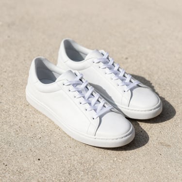Close-up of classic white minimalist sneakers on a sandy concrete floor, soft natural lighting
