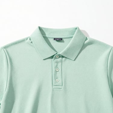 Clean shot of a pastel green cotton polo shirt, neatly styled, soft island daylight