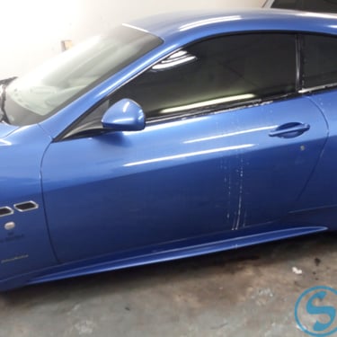 : Mėlynas „Maserati GranTurismo“ su juodais ratlankiais ir tamsintais stiklais, pastatytas garaže.