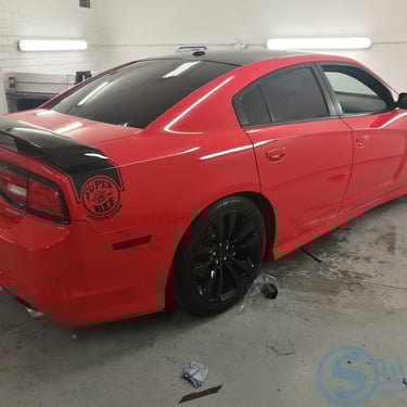 Raudono „Dodge Charger“ su tamsintais langais nuotrauka garaže.