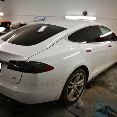 Balta „Tesla Model S“ su tamsintais langais stovi garaže.