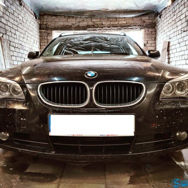 Juodas BMW 5 serijos (E60) automobilis garaže, kurio žibintai reikalauja