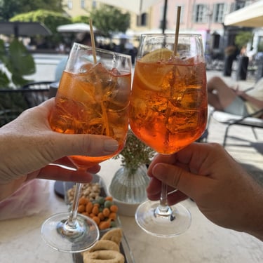 Two Aperol spritz cocktails being toasted with snacks during aperitivo