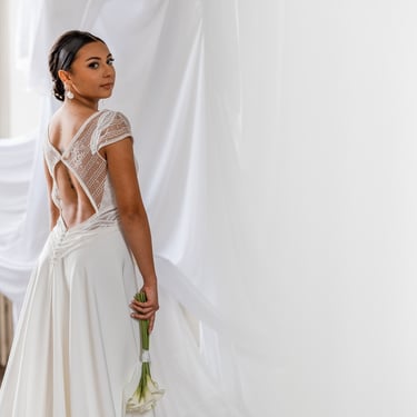 Une femme de dos en robe de mariée blanche un bouquet de fleurs à la main