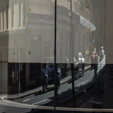 Reflection on curved glass showing a distorted city street under sunlight, creating a surreal urban scene.