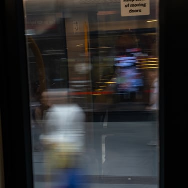 View through a moving tram's door. Outside, abstract streaks of light and indistinct figures create a sense of motion.