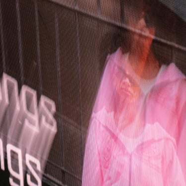 A person in a pink jacket is overlaid with a man on a surface in a store. The background creates an abstract effect.
