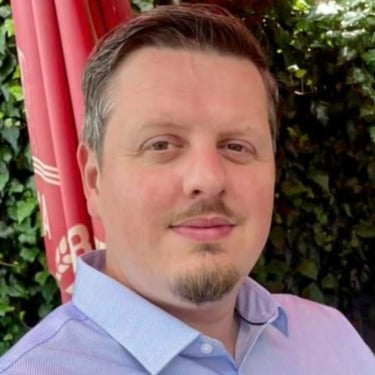 Dean Constantine, a white male, with brown eyes, hair and beard, in a blue collared shirt