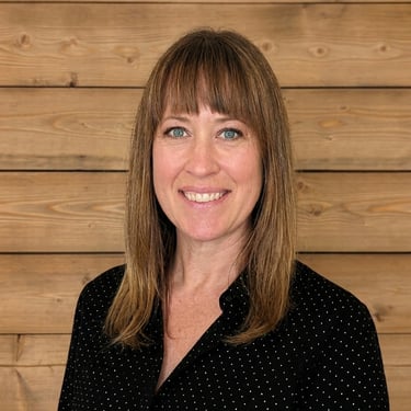 Professional headshot of a smiling woman with brown hair against a rustic wood plank background.
