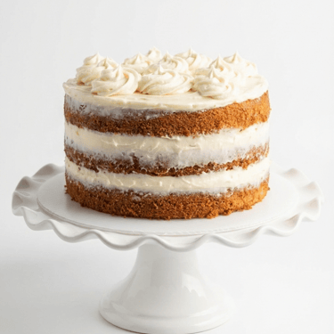 Homemade 3-layer carrot cake with cream cheese frosting swirls on a white cake stand