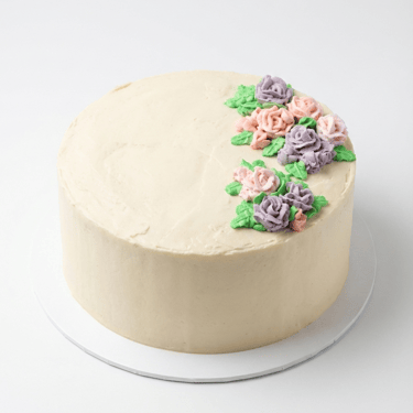 Custom buttercream cake with smooth white frosting and pastel pink and purple floral design for birthdays in Decatur TX