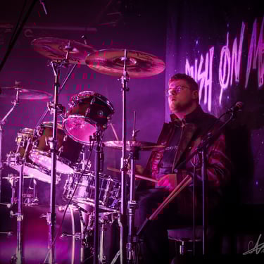  arthur debary le batteur jouant de la batterie lors du faster than light festival illuminé d'un spot rose, devant notre logo