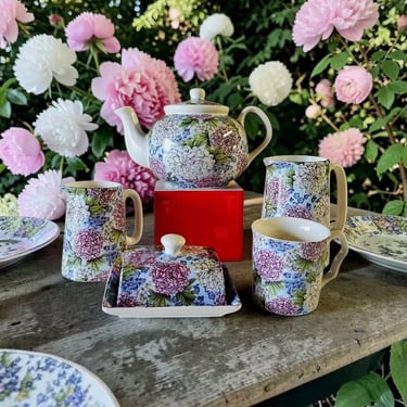 Teapot and other ceramics featuring a floral pattern, on a table surrounded by flowers