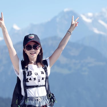 Mulher jovem fazendo sinal de paz com a mão, sorrindo na frente de montanhas