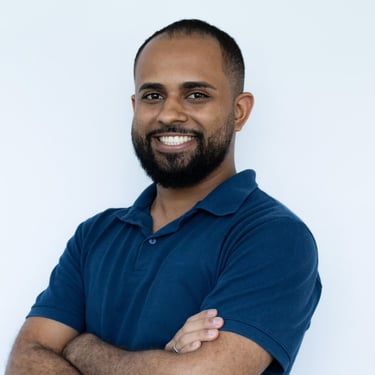 Foto do autor da matéria Igor Souza, sorrindo, com os braços cruzados, blusa polo azul escuro e pare