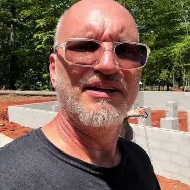 A man wearing sunglasses standing in front of a residential concrete block foundation at a construction site.
