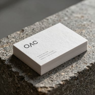 A minimalist stack of textured cotton business cards resting on a weathered stone block under diffused daylight.