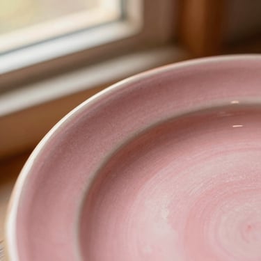Macro detail of a hand-painted pink ceramic plate edge, showing the textured clay and glossy glaze, warm sunlight