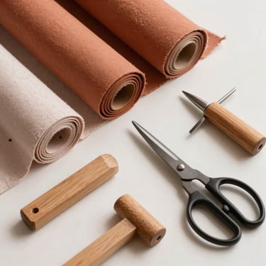 Flat-lay of natural terracotta and blush linen fabric rolls, wooden tailoring tools, and scissors on a clean light surface, bright morning light