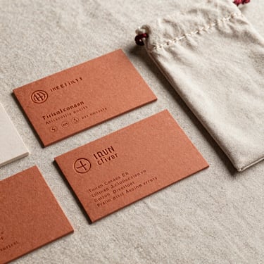 A finished brand identity package resting on raw linen, featuring custom terracotta business cards and a hand-stamped linen pouch under soft directional light.