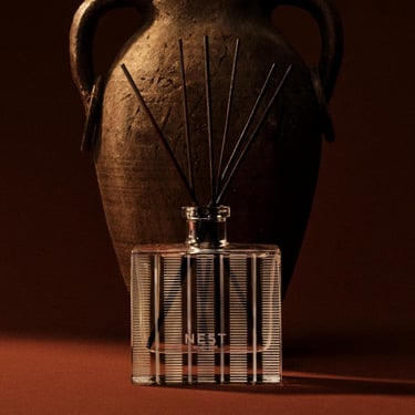 NEST New York glass reed diffuser set in front of a rustic antique clay amphora vase.