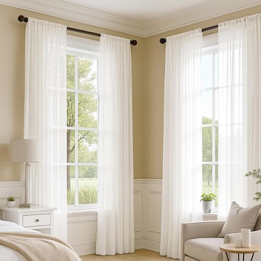 Elegant white sheer curtains on black rods framing large windows in a bright, modern bedroom.
