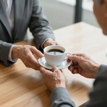 Close-up of a friendly consultant's hands offering a warm cup of coffee to an older client over a clean wooden table. Soft natural light, focus on the welcoming gesture, professional and caring atmosphere.