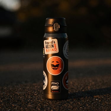 A black Contigo thermos covered in custom stickers, warm sunset light.