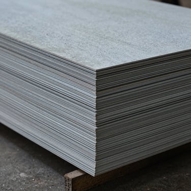 Stacked raw architectural veneer sheets in a cool-toned warehouse bay, showing precise edge-cutting and uniform thickness.