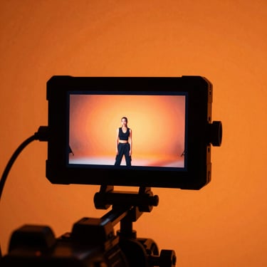 Behind-the-scenes video shoot, camera monitor displaying high-contrast campaign footage, warm orange backlight