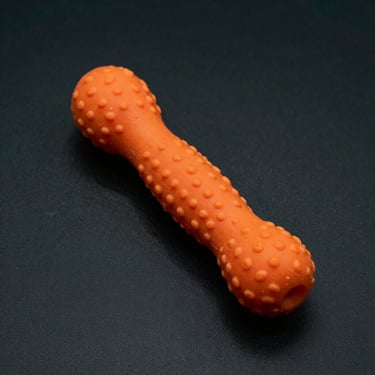 Studio shot of an orange textured rubber chew toy designed for aggressive chewers, dark background