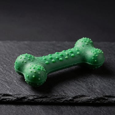 A durable natural rubber chew toy shaped like a textured bone, resting on a dark slate surface, dramatic lighting