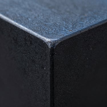 Macro shot of blackened steel finish, showing deep blue and charcoal grey variations with a soft matte luster.