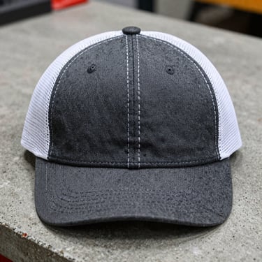 Front-facing product shot of a Richardson 112 cap in charcoal and white mesh, sitting on a concrete workbench, sharp macro detail, 50mm lens